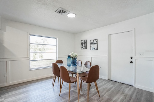 dining area featuring visible vents, a textured ceiling, a wainscoted wall, and light wood finished floors