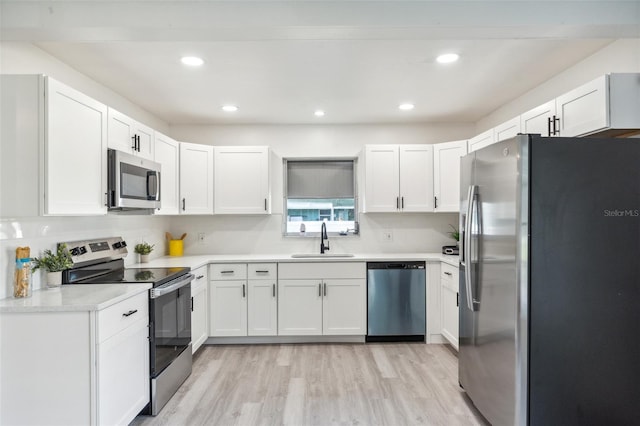 kitchen featuring light wood-type flooring, a sink, white cabinetry, appliances with stainless steel finishes, and light countertops