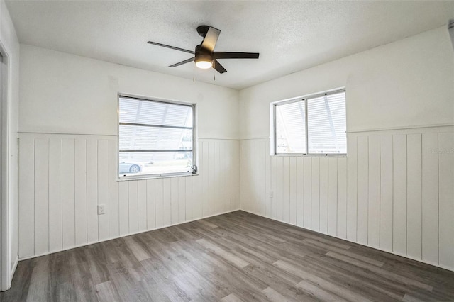 unfurnished room featuring a textured ceiling, ceiling fan, dark hardwood / wood-style flooring, and wood walls