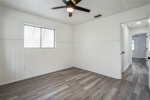 empty room featuring ceiling fan, visible vents, a wainscoted wall, and wood finished floors