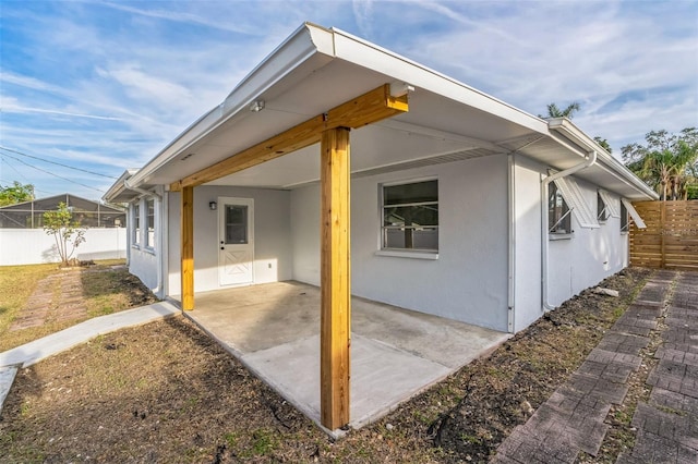 view of side of home with a patio area, fence, and stucco siding