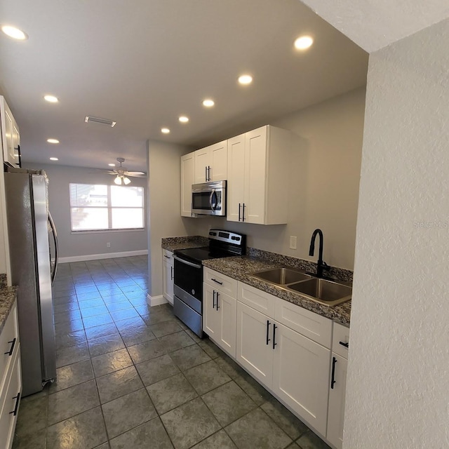 kitchen featuring baseboards, a sink, ceiling fan, stainless steel appliances, and white cabinetry