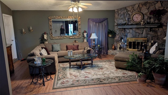 living room featuring hardwood / wood-style floors, ceiling fan, a stone fireplace, and a textured ceiling