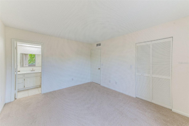 unfurnished bedroom featuring sink, light carpet, and a closet