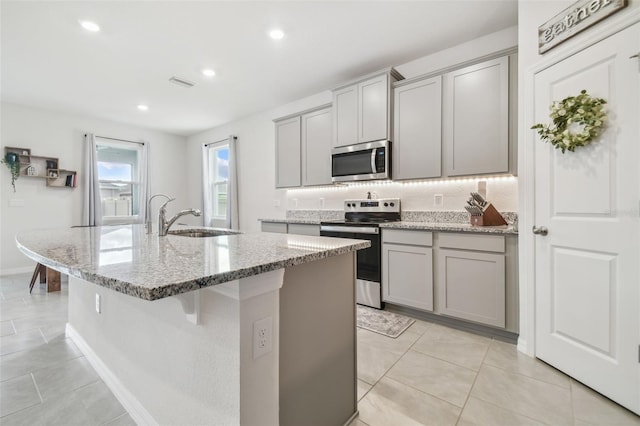 kitchen with stainless steel appliances, a kitchen island with sink, gray cabinetry, and sink