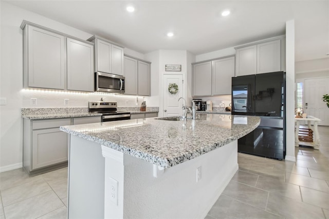 kitchen featuring light stone counters, gray cabinetry, stainless steel appliances, a kitchen island with sink, and sink