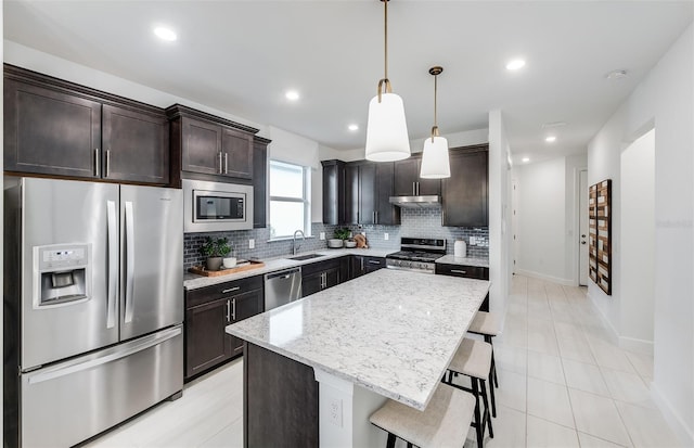 kitchen with sink, stainless steel appliances, pendant lighting, a breakfast bar, and a kitchen island