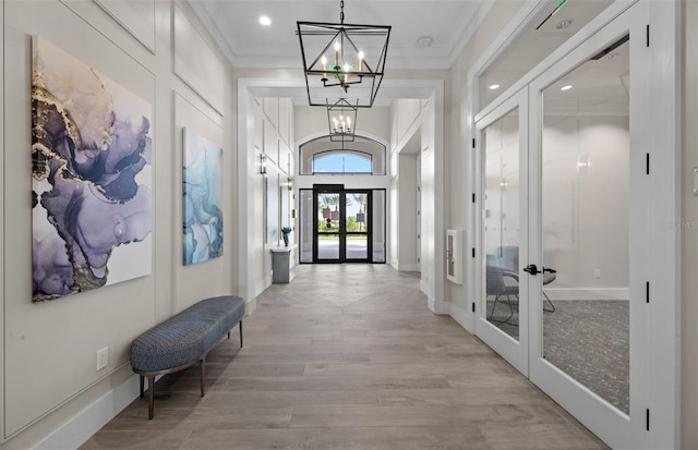 hall featuring crown molding, baseboards, light wood-style flooring, french doors, and a notable chandelier