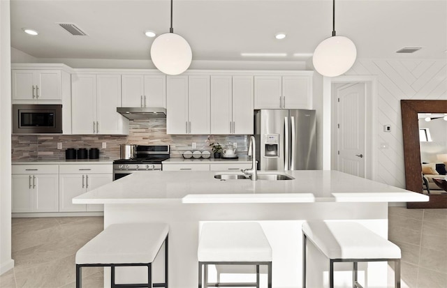 kitchen featuring a sink, stainless steel appliances, tasteful backsplash, and a center island with sink