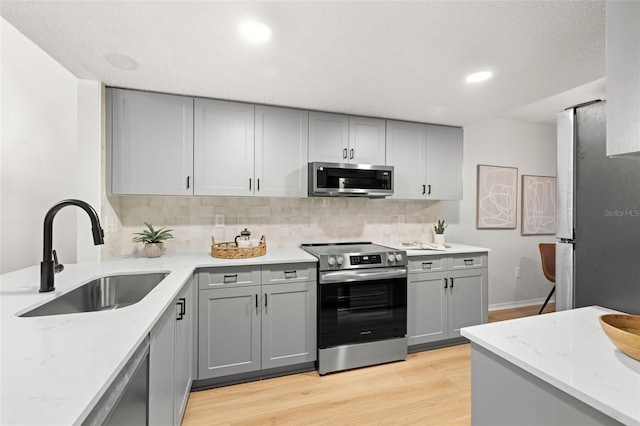 kitchen featuring appliances with stainless steel finishes, light wood-type flooring, backsplash, and sink