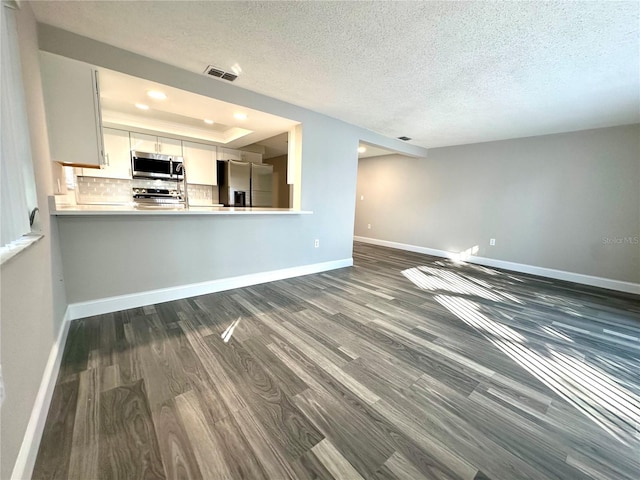 unfurnished living room featuring a textured ceiling, a raised ceiling, and dark wood-type flooring