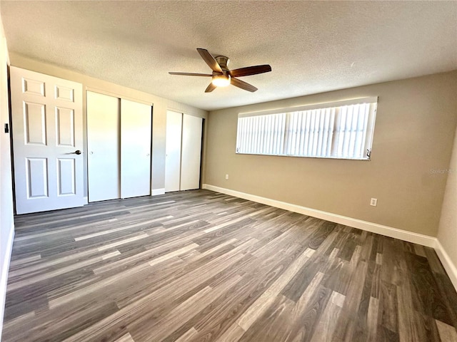 unfurnished bedroom with a textured ceiling, dark hardwood / wood-style flooring, ceiling fan, and multiple closets