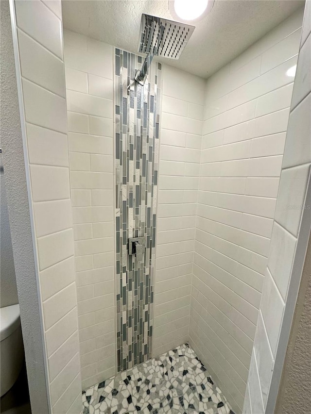 bathroom featuring toilet, a tile shower, and a textured ceiling