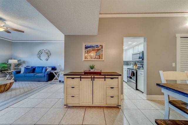 kitchen with light tile patterned floors, stainless steel appliances, a textured ceiling, and ornamental molding