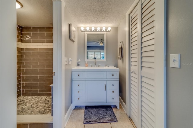 bathroom featuring vanity, tile patterned flooring, ceiling fan, tiled shower, and a textured ceiling