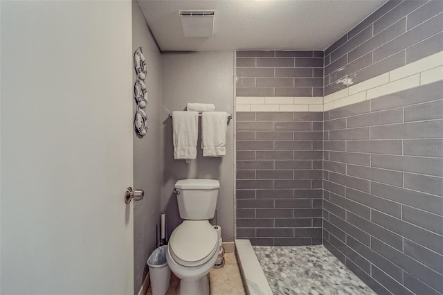 bathroom with a tile shower, tile patterned floors, a textured ceiling, and toilet