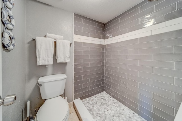 bathroom featuring a tile shower, a textured ceiling, and toilet