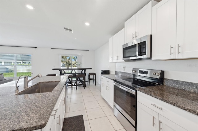 kitchen featuring sink, white cabinetry, stainless steel appliances, and dark stone counters