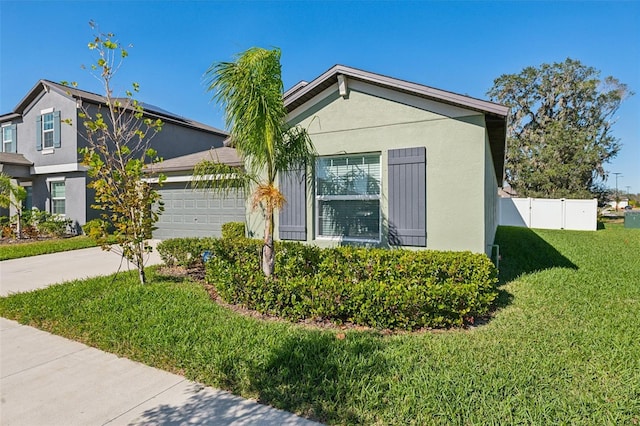 view of side of property with driveway, a garage, fence, a yard, and stucco siding