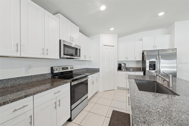 kitchen with appliances with stainless steel finishes, white cabinets, a sink, and dark stone countertops