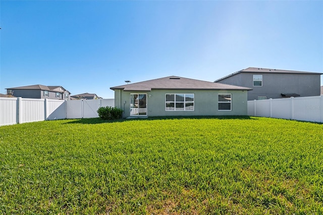 back of house with a fenced backyard, a lawn, and stucco siding