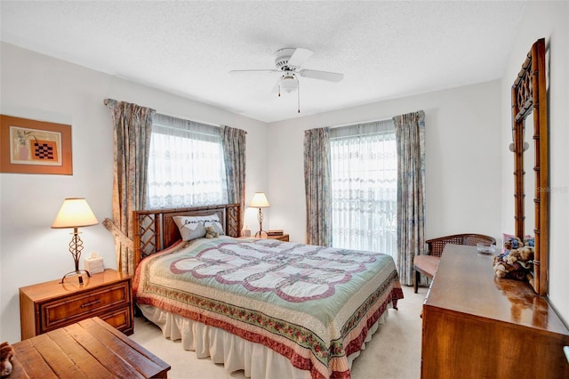 bedroom with a textured ceiling, light colored carpet, multiple windows, and ceiling fan