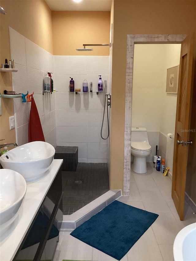 bathroom featuring vanity, a shower, tile walls, tile patterned flooring, and toilet