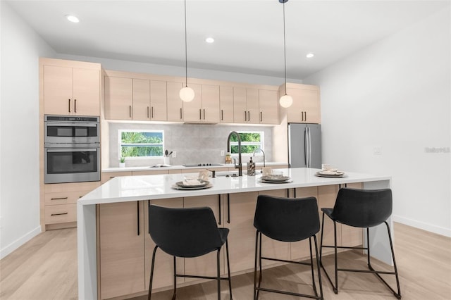 kitchen with pendant lighting, a kitchen island with sink, light brown cabinetry, light hardwood / wood-style floors, and stainless steel appliances