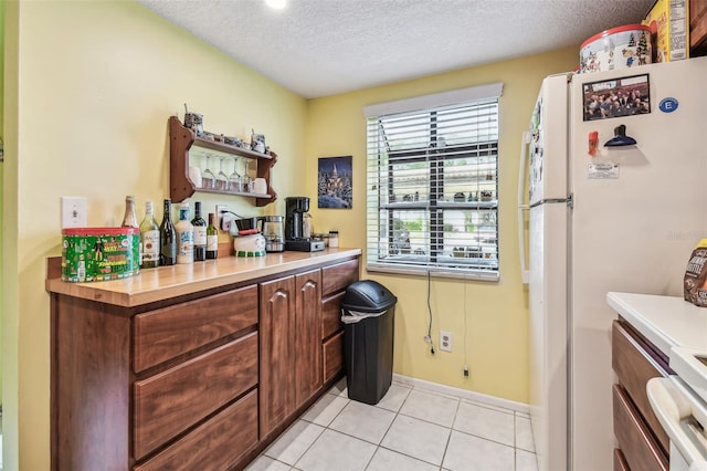 kitchen featuring light tile patterned floors, white fridge, stainless steel stove, and a textured ceiling