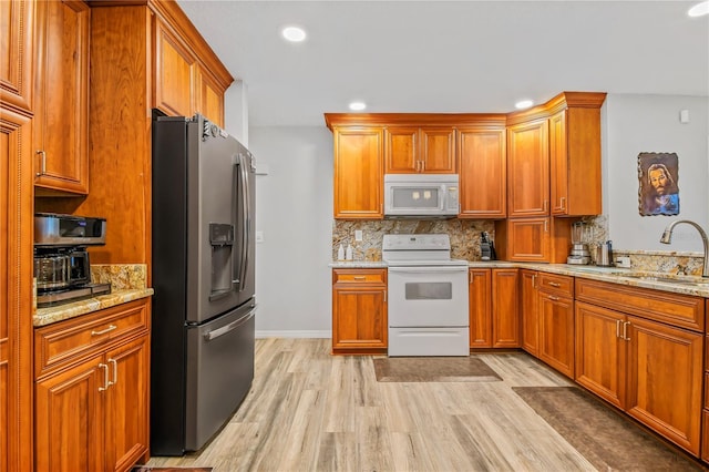 kitchen featuring light stone countertops, tasteful backsplash, white appliances, sink, and light hardwood / wood-style floors