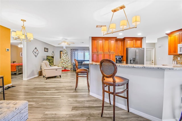 kitchen with a breakfast bar, ceiling fan with notable chandelier, stainless steel fridge, light wood-type flooring, and decorative light fixtures