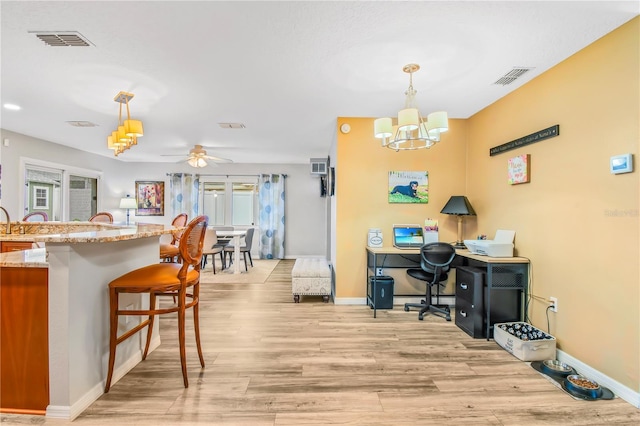 kitchen with light hardwood / wood-style flooring, hanging light fixtures, a breakfast bar area, light stone counters, and ceiling fan with notable chandelier