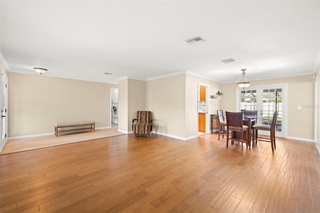 dining room featuring washer / dryer, french doors, ornamental molding, and light wood-type flooring