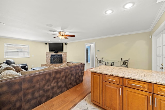 kitchen with ceiling fan, light stone counters, crown molding, and light hardwood / wood-style flooring