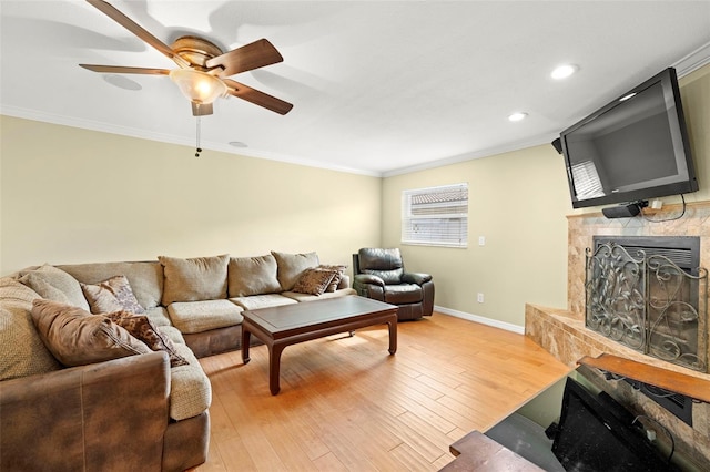 living room with hardwood / wood-style flooring, a stone fireplace, ceiling fan, and crown molding