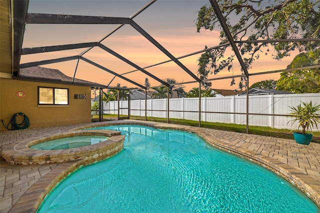 pool at dusk with an in ground hot tub, glass enclosure, and a patio area