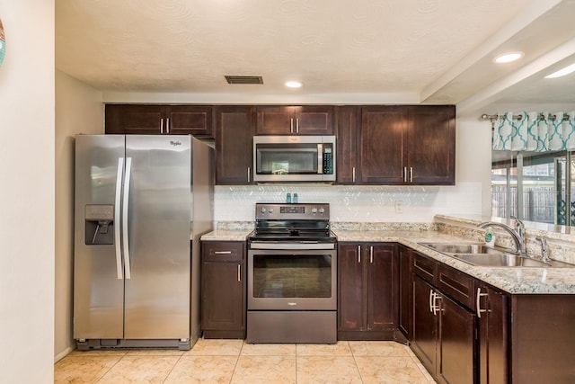 kitchen featuring sink, light stone countertops, tasteful backsplash, dark brown cabinets, and stainless steel appliances