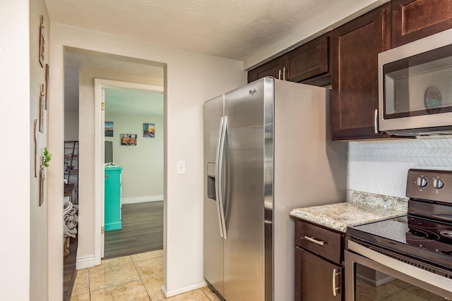 kitchen with light stone countertops, light wood-type flooring, dark brown cabinets, a textured ceiling, and stainless steel appliances