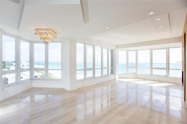 unfurnished sunroom with a raised ceiling, a water view, and an inviting chandelier