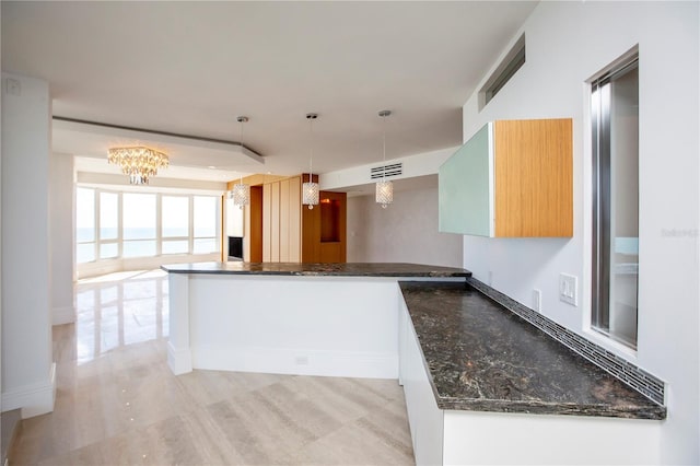 kitchen featuring kitchen peninsula, pendant lighting, a notable chandelier, and dark stone countertops