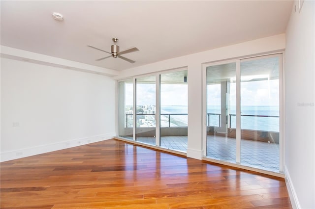 spare room with ceiling fan, a water view, and wood-type flooring