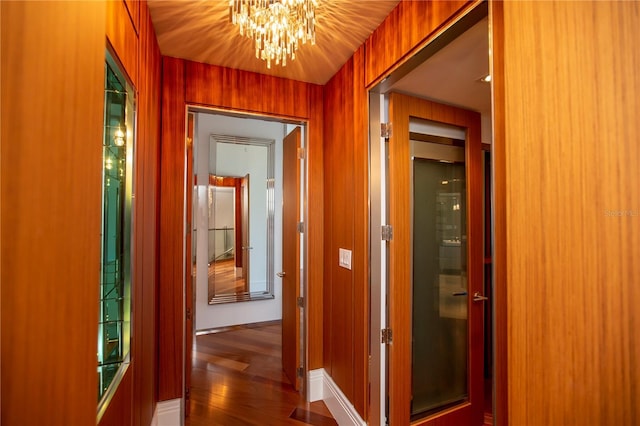 corridor featuring a notable chandelier, wood walls, and dark wood-type flooring