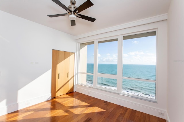 unfurnished room featuring a water view, hardwood / wood-style flooring, and ceiling fan