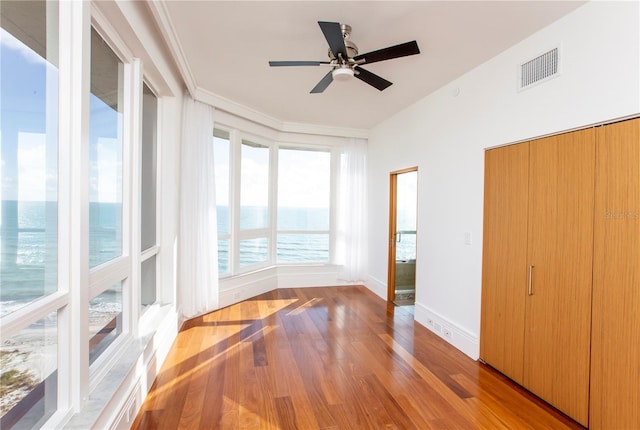 unfurnished sunroom featuring ceiling fan and a water view