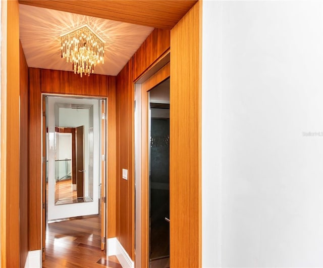 hall with wooden walls, hardwood / wood-style floors, and a notable chandelier