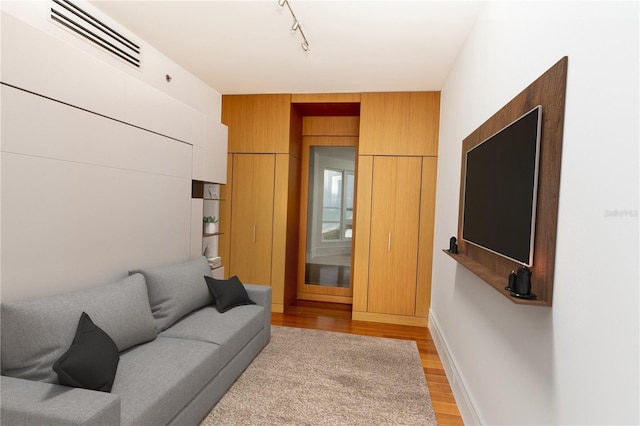 living room with light wood-type flooring, wooden walls, and track lighting