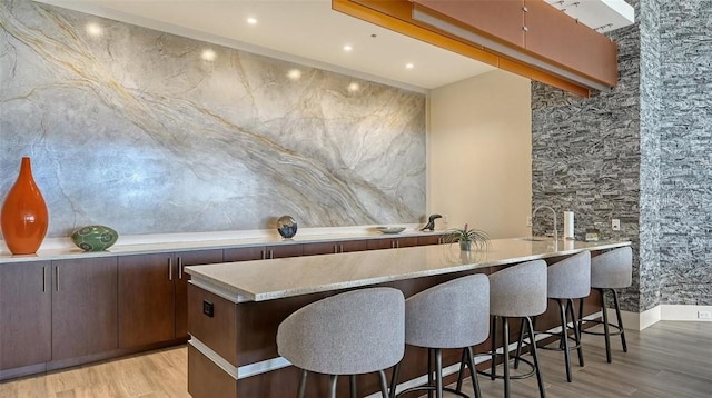 bar featuring light stone counters, dark brown cabinets, and light hardwood / wood-style floors