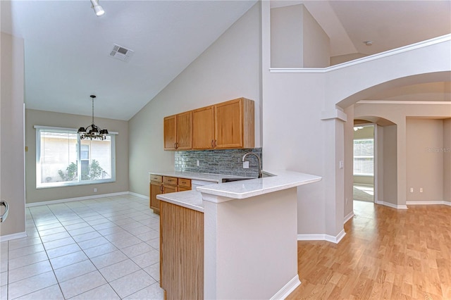 kitchen with backsplash, sink, high vaulted ceiling, a chandelier, and hanging light fixtures