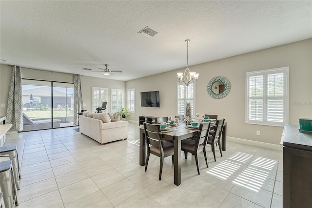 dining space with a textured ceiling, ceiling fan with notable chandelier, a wealth of natural light, and light tile patterned flooring