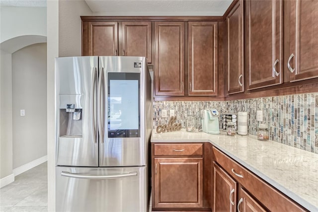 kitchen with decorative backsplash, light tile patterned flooring, light stone counters, and stainless steel refrigerator with ice dispenser